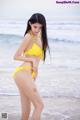 A woman in a yellow bikini standing on the beach.