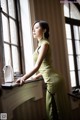 A woman in a green dress leaning against a window.