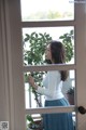 A woman standing in front of a window looking out the window.