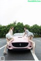 A couple of women standing next to a pink car.