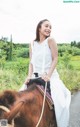 A woman in a white dress riding a brown horse.