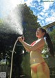 A woman in a bikini is spraying water from a hose.