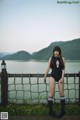 A woman in a black bathing suit standing by a fence.