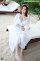 A woman in a white dress sitting on a beach.